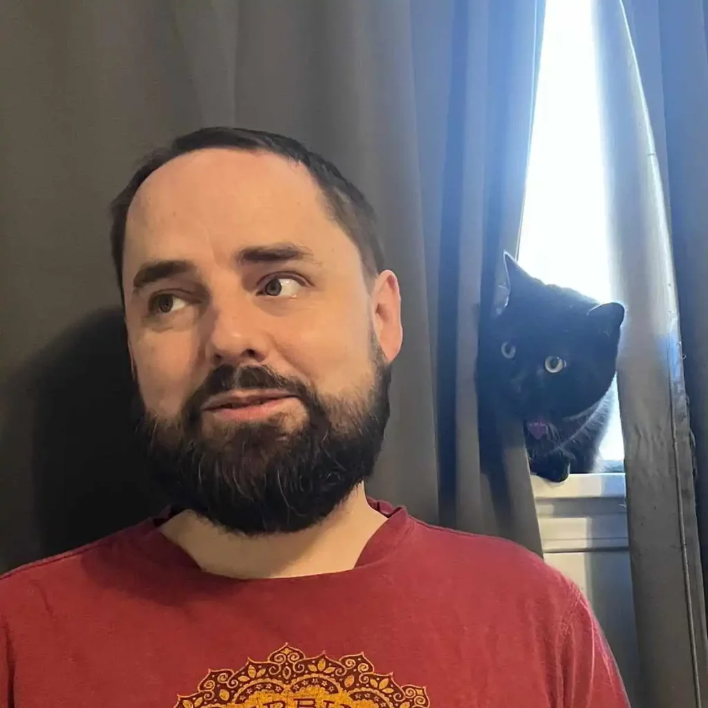 Image contains a photo of Toronto cat sitter, Ryan Patey, looking away from a black cat sitting on a window sill.